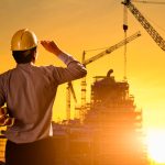 Silhouette engineer wear a helmet at construction site with crane background and sunset